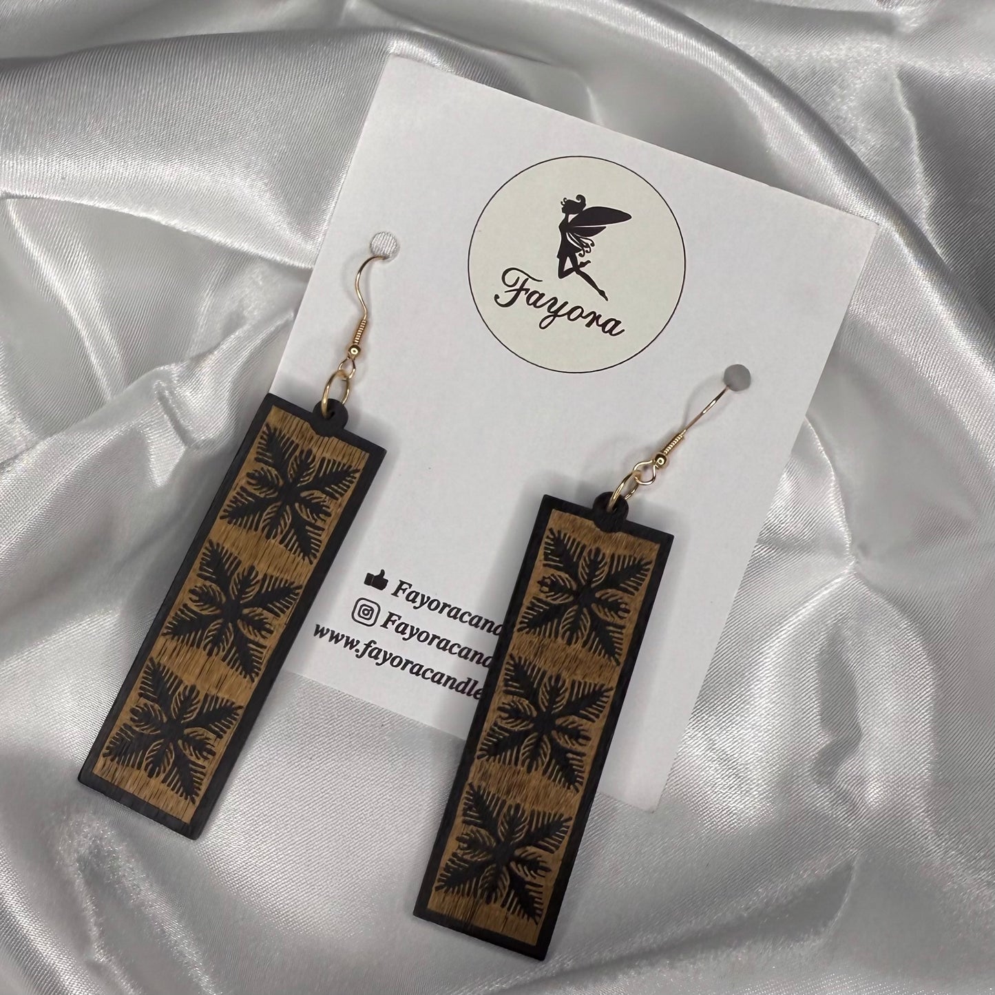 Wooden earrings with floral patterns on a white card with 'Fayora' branding, set against a satin background.