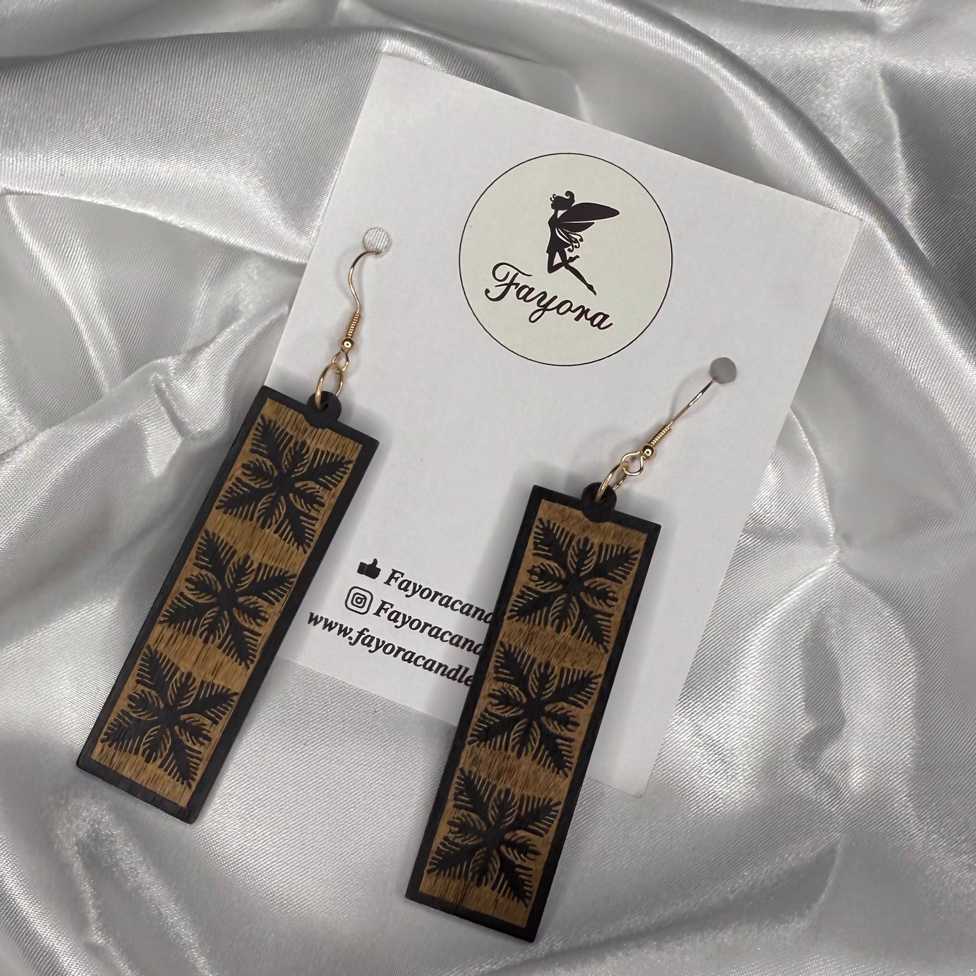 Wooden earrings with floral patterns on a white card with 'Fayora' branding, set against a satin background.