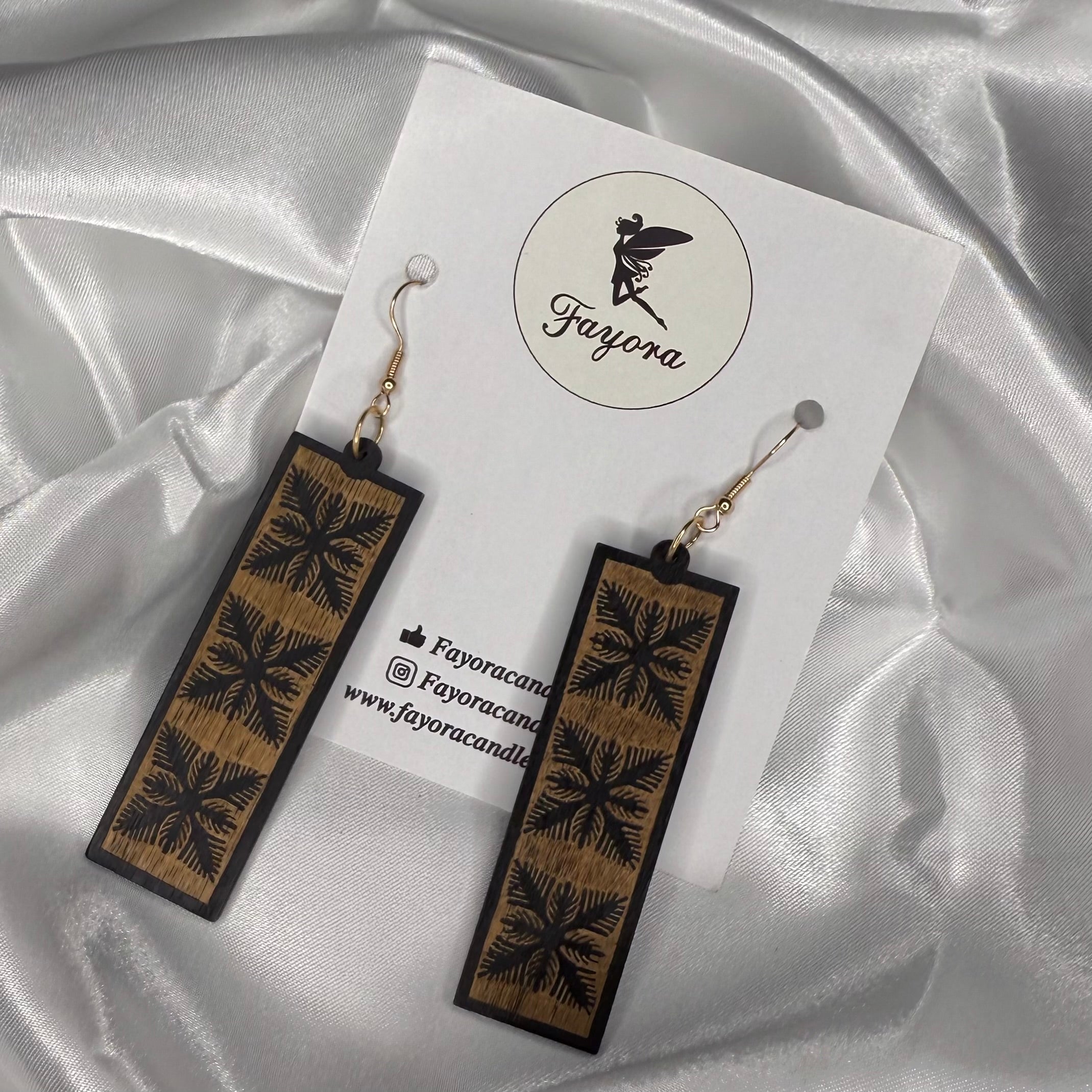 Wooden earrings with floral patterns on a white card with 'Fayora' branding, set against a satin background.