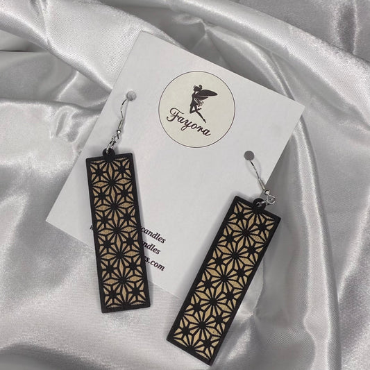 Pair of black and gold geometric earrings on a white card with 'Fayora' branding, against a satin fabric background.